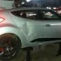 Hyundai Veloster prata estacionado em pátio automotivo.