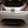 Traseira de um Hyundai Veloster prata estacionado em pátio automotivo.