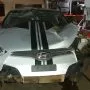 Frente de um Hyundai Veloster prata estacionado em pátio automotivo.