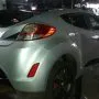 Traseira de um Hyundai Veloster prata estacionado em pátio automotivo.