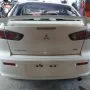 Traseira de um Lancer branco estacionado em pátio automotivo.