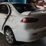 Traseira de um Lancer branco estacionado em pátio automotivo.