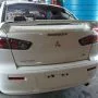 Traseira de um Lancer branco estacionado em pátio automotivo.