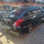 Traseira de um Nissan Versa preto estacionado em pátio automotivo.