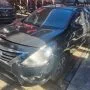 Frente de um Nissan Versa preto estacionado em pátio automotivo.