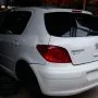 Traseira de um Peugeot 307 branco estacionado em pátio automotivo.